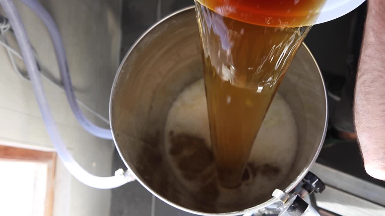 Inquadratura dall'alto al rallentatore di un uomo che versa birra in un fermentatore per avviare il processo di fermentazione