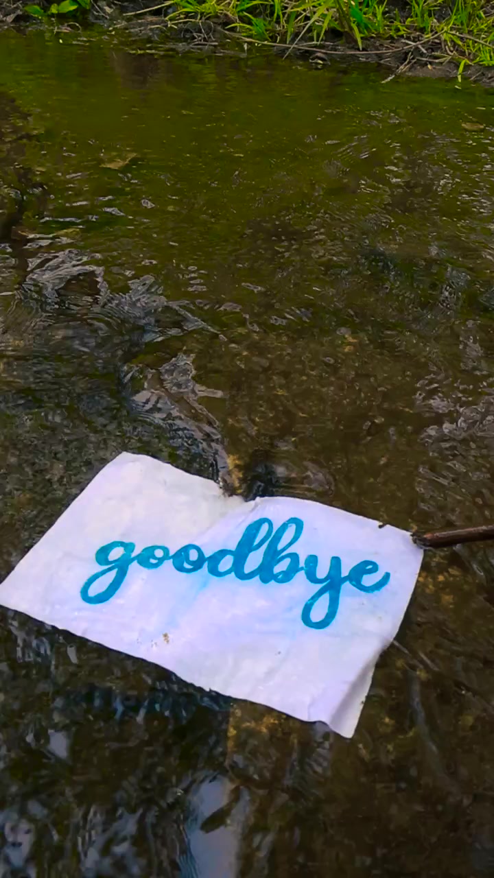Symbolic concept of farewell showing a goodbye letter floating downstream in a river. The handwritten note moves with the water current