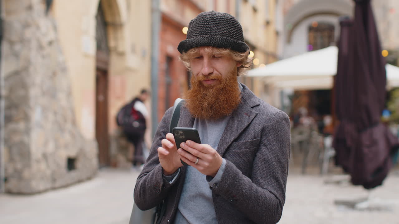 젊은 남자가 스마트폰을 사용하고 문자 메시지를 입력하고 인터넷을 탐색하고 카메라를 보고 일을 마치고 있습니다.