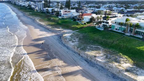 aerial footage captures beachfront homes along gold coast, australia, with waves gently lapping the shore under clear skies