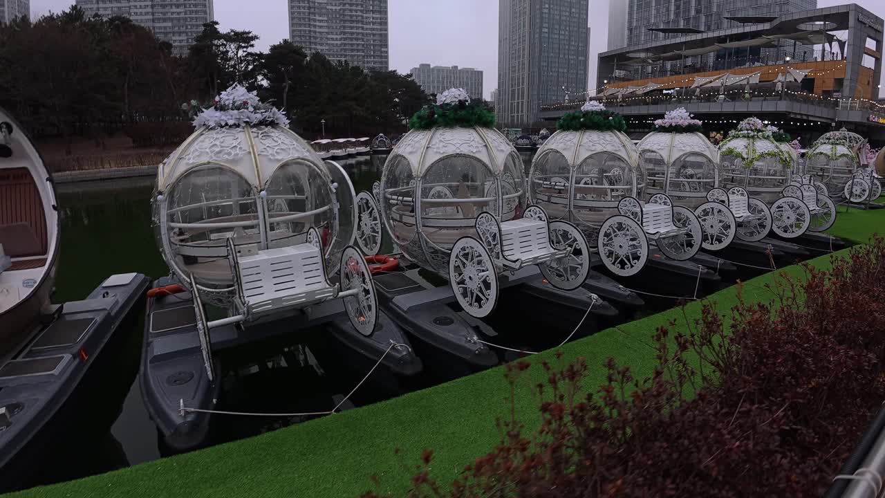 Walking On Promenade With View Of Pedalo And Decorative Carriage-like Boats Docked On Waterway. Songdo Central Park In Incheon. POV