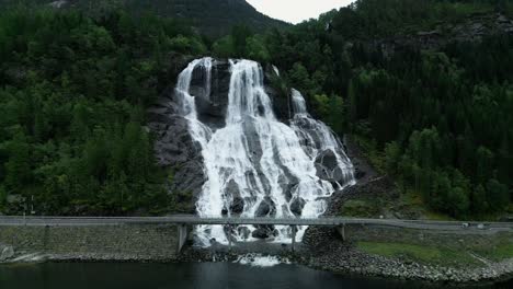 norwegian road in front of a wild waterfall that flows into the fjords of the norse sea