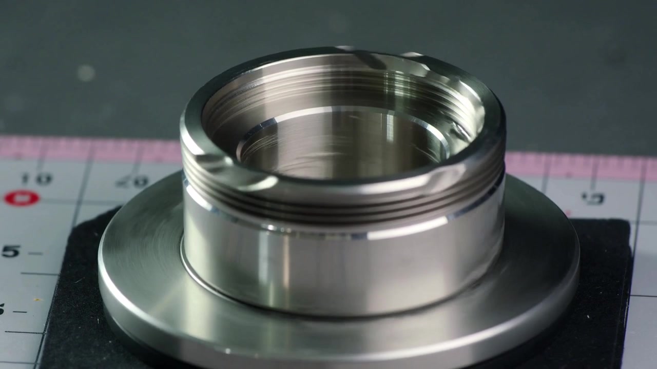 Rotating metal cylinder showing threaded bore and rim notches on pad and ruler mat for inspection