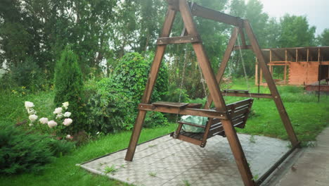 tambor de agua de plástico lleno de agua y banco de columpios de madera al aire libre que sostiene una bolsa de color menta, el fondo presenta un jardín exuberante con vegetación, flores y árboles