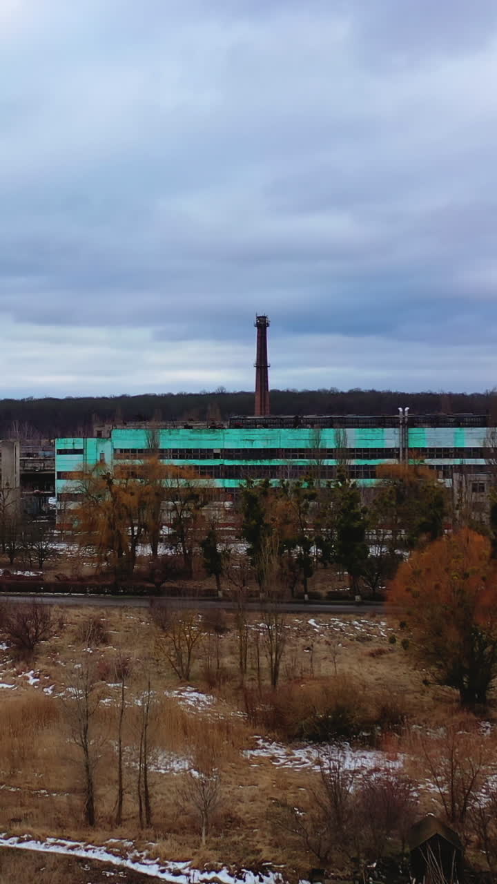 Old ruined factory among nature. Front view of a large ruined buildings of abandoned plant under gray sky. Vertical video