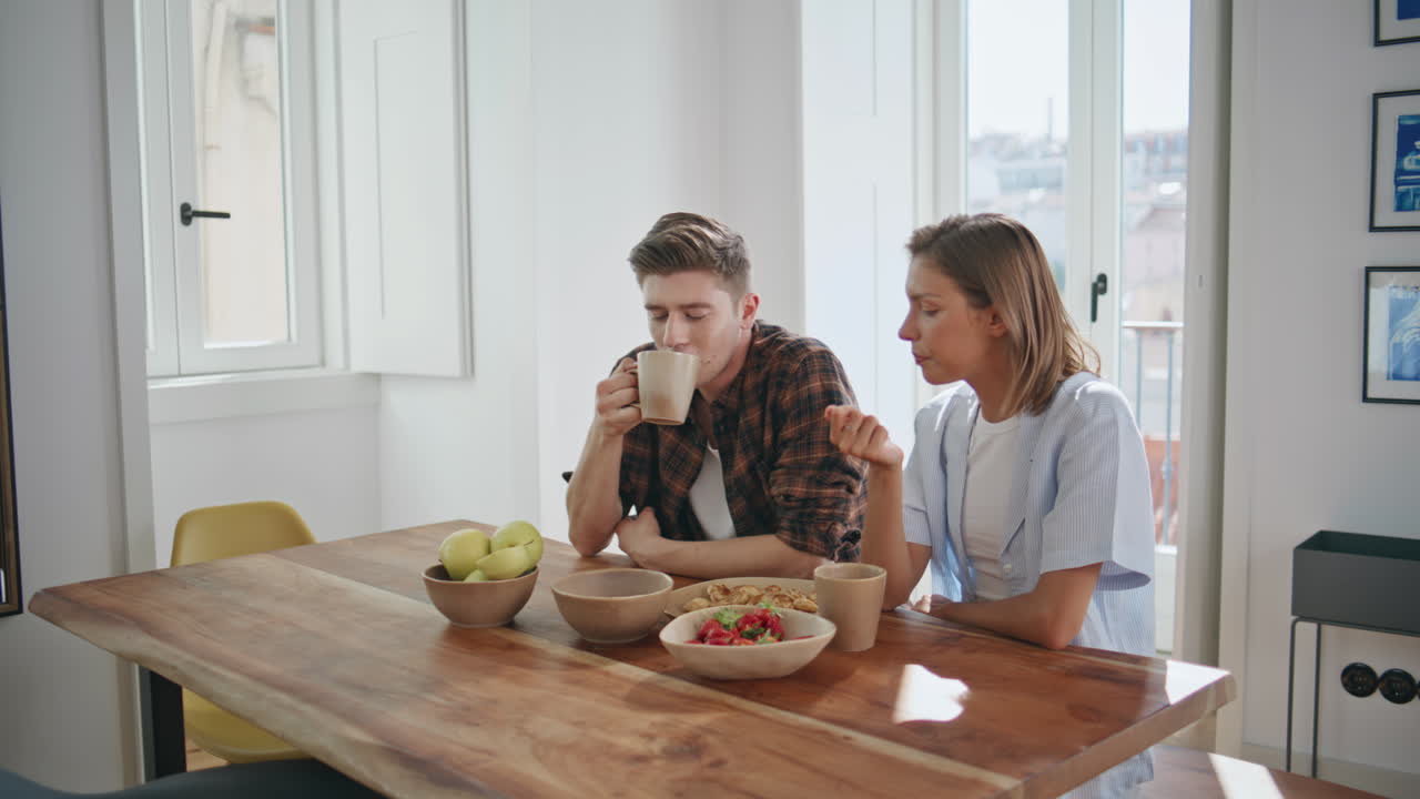Laughing couple resting home enjoying breakfast. Carefree young people talking