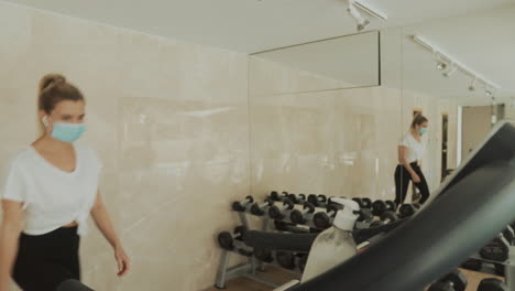 young athlete woman with face mask uses an exercise machine and hand sanitizer in the gym