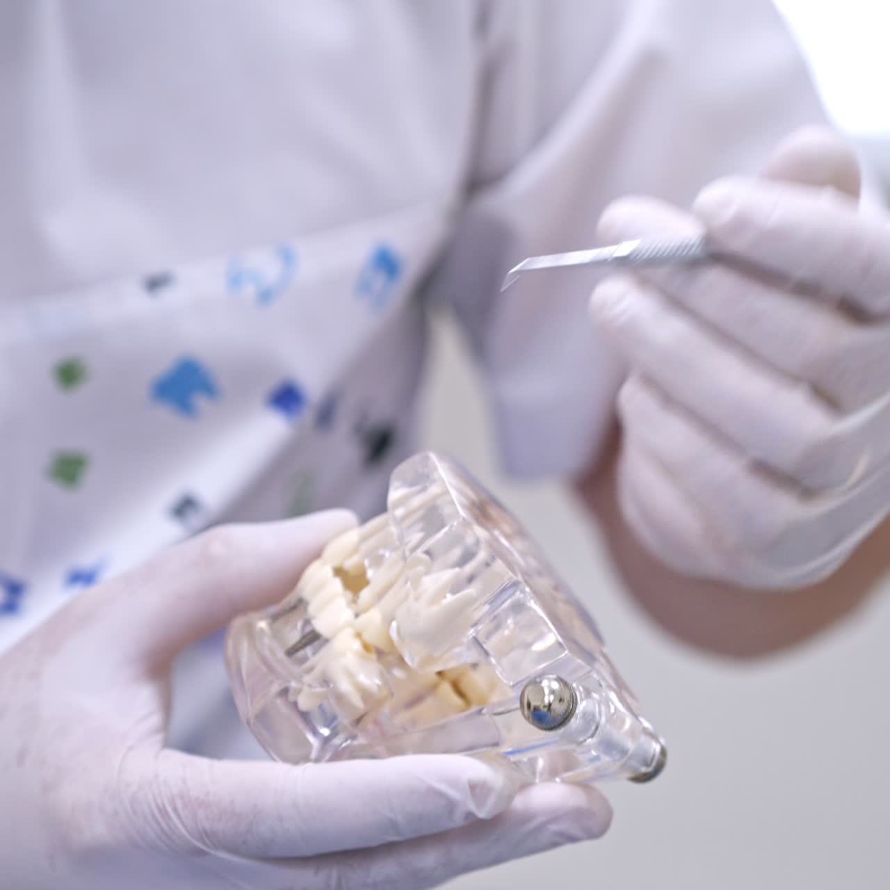 Doctor shows on a plastic jaw sample or model different methods of teeth treatment. Modern dental clinic background. Health concept. White medical gloves on male doctor's hands.