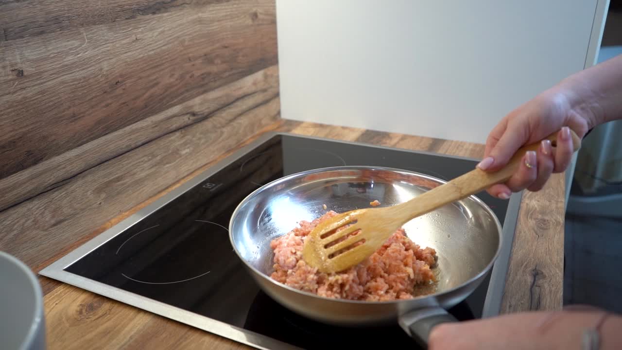 wodden 스푼으로 프라이팬에 다진 고기를 휘젓는 여자