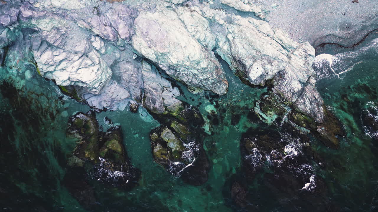 Ocean current waves break on rocky shoreline with algae covered rocks in Newport