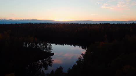 Fliegen-Bei-Sonnenuntergang-über-Dunklem-Wald,-Während-Sich-Der-Himmel-Aus-Rosa-Wolken-Im-See-Widerspiegelt