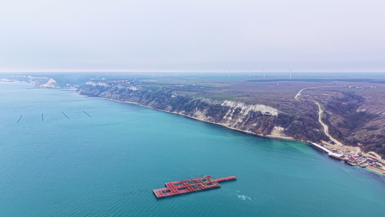 Fazenda de mexilhões localizada no mar perto de uma área costeira com falésias e água azul clara durante o dia