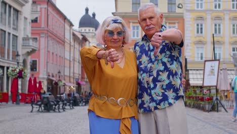 upset senior man woman showing thumbs down sign gesture, expressing discontent, disapproval, dislike