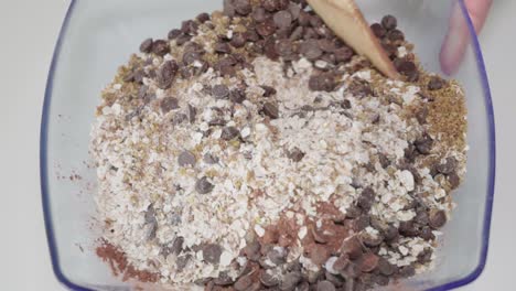 Mixing-dry-oatmeal-cookie-ingredients-in-bowl-with-wooden-spoon,-Overhead