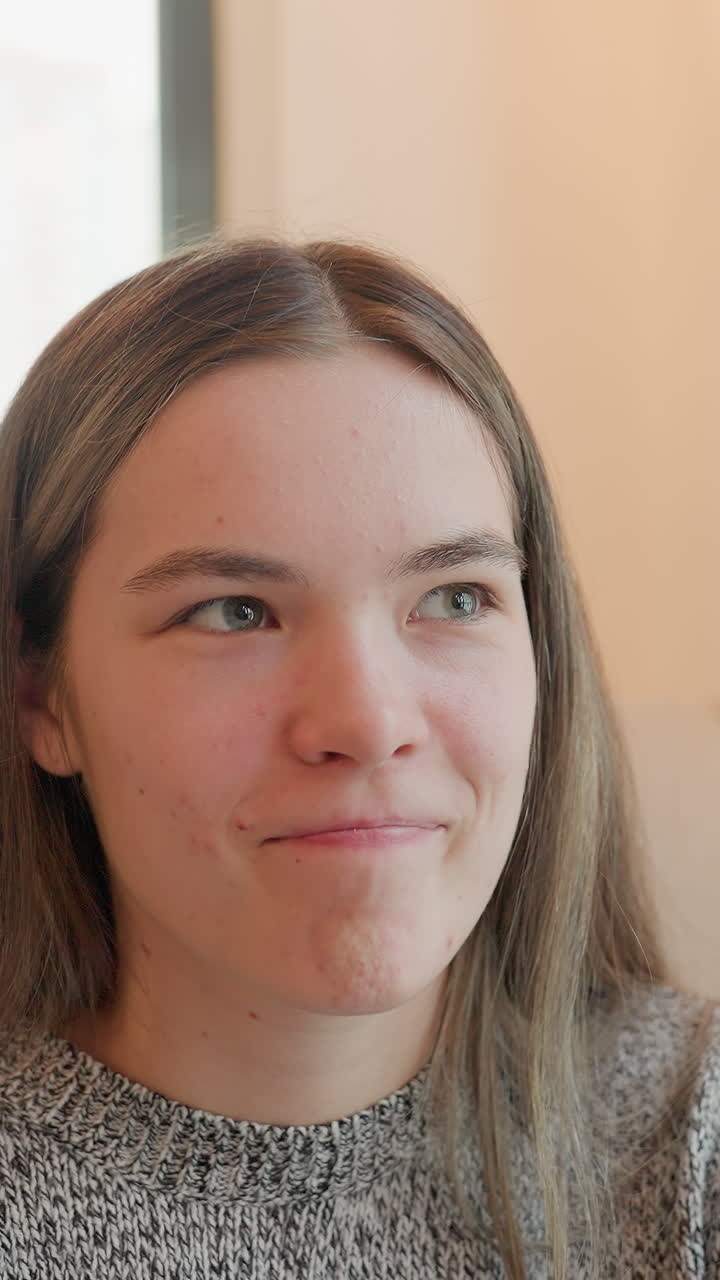 Pensive caucasian woman sly smile indoors near window with warm amber light, offering sideways glances and subtle smirks expression shifts from thoughtful to mischievous, suggesting curious teen