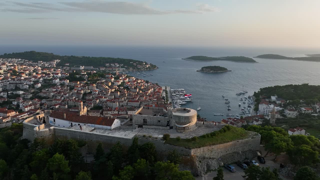 Panoramic Of Fortica Fortress At Hilltop With Red-Roof Houses On Adriatic Coast At Background In Hvar, Croatia. Aerial Shot