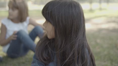 retrato de una linda chica de pelo largo sentada en el parque con amigos y mirando alrededor