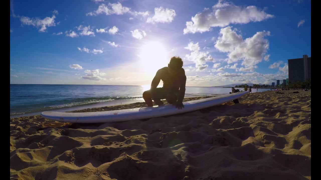 Surfer with a surfboard sitting on the beach 4k