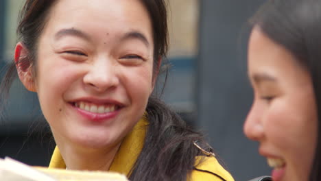 close up of two young female friends sitting on steps eating hot dogs bought at street food market stall 2