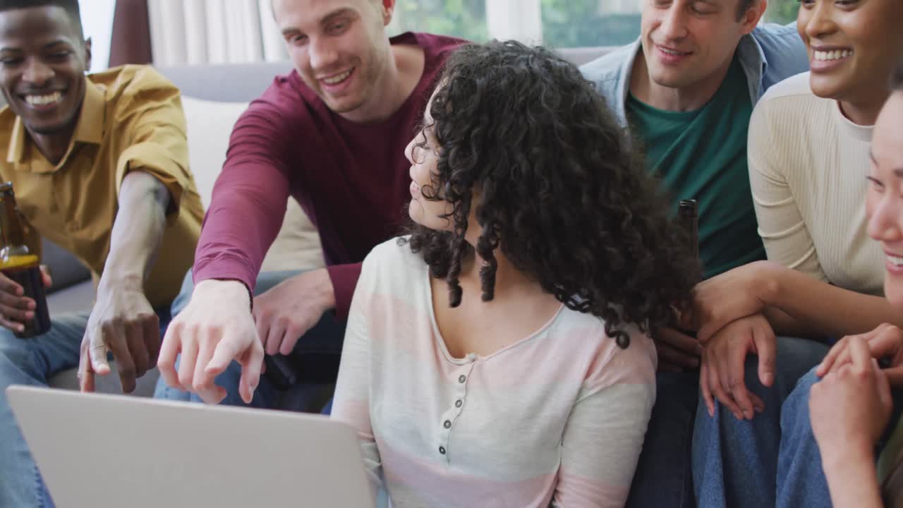 Diverse group of happy male and female friends looking at laptop and talking in living room