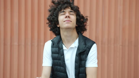 teenager with curly hair in front of an orange wall