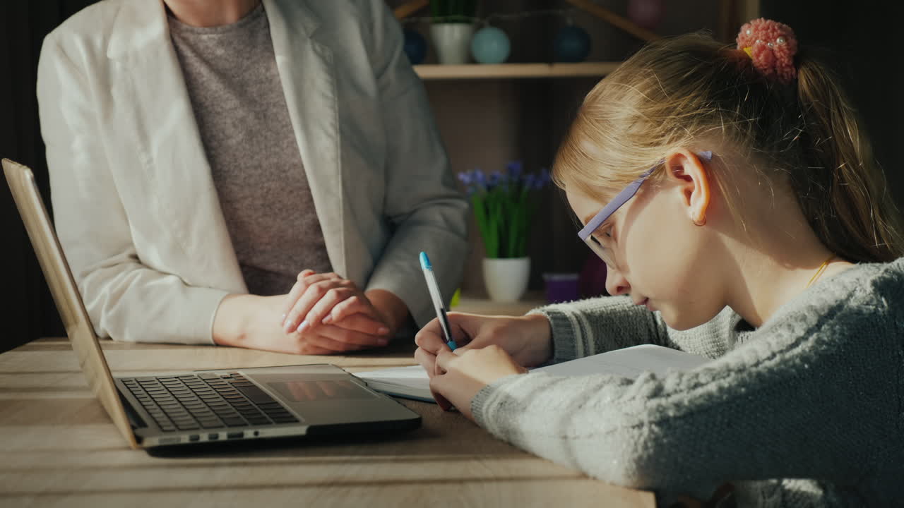 la mujer ayuda al niño con la tarea mientras la niña estudia cerca de una computadora portátil