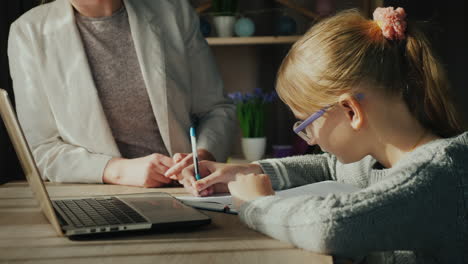 la mujer ayuda al niño con la tarea mientras la niña estudia cerca de una computadora portátil