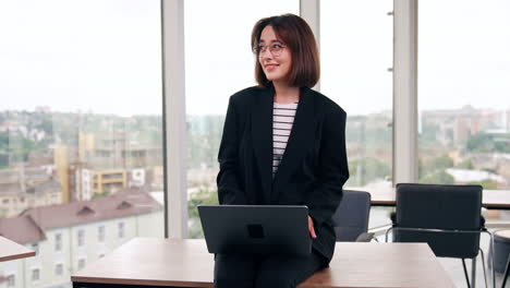 brunette girl sitting on the desk types on her laptop. portrait of a positive modern lady working remote.
