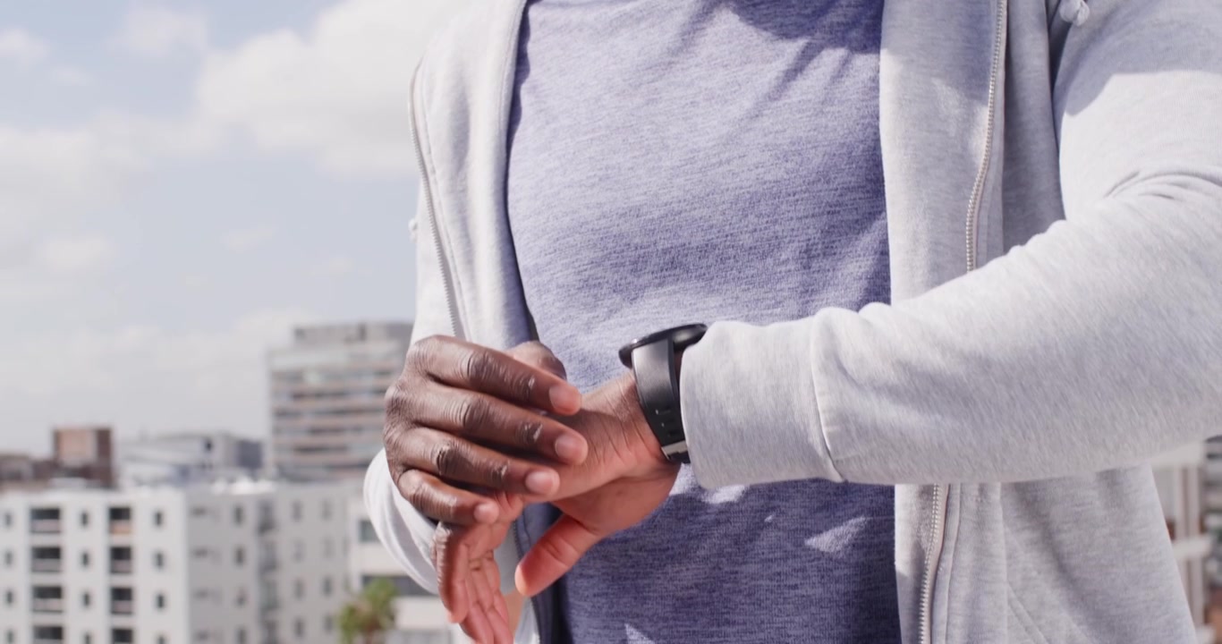 Afroamerikansk mand reagerer på smartwatch-notifikation, tapper og swiper på tagterrasse