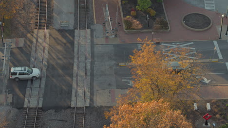 Vista-Aérea-De-Los-Autos-Que-Cruzan-Las-Vías-Del-Tren-En-Una-Intersección-En-Kirkwood-Missouri-En-Otoño-A-La-Hora-Dorada