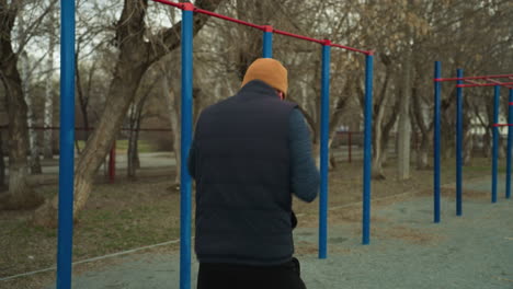 back view of a coach working out fast in an outdoor gym, with blurred views of a car passing across the road, with red and blue iron bars visible in the background