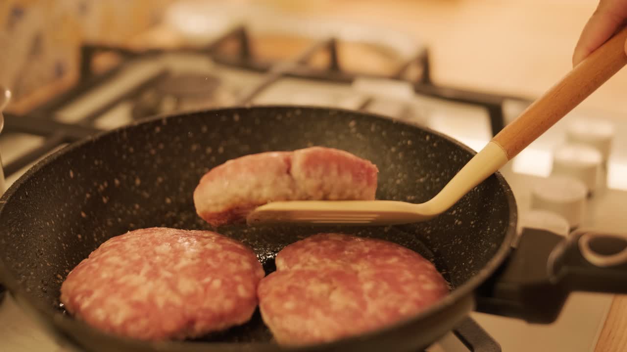 Raw meat patties frying in pan on kitchen stove