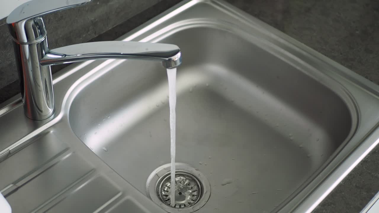 Primer plano de agua corriendo en un fregadero de cocina de acero inoxidable