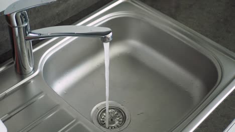 primer plano del agua que entra en un fregadero de cocina de acero inoxidable