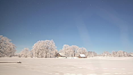 Stars-crossing-the-sky-above-a-cabin,-frozen-lake,-and-winter-landscape---wide-angle-time-lapse