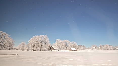 stars crossing the sky above a cabin, frozen lake, and winter landscape - wide angle time lapse