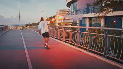 back view of young guy riding skateboard with signal fire on bridge