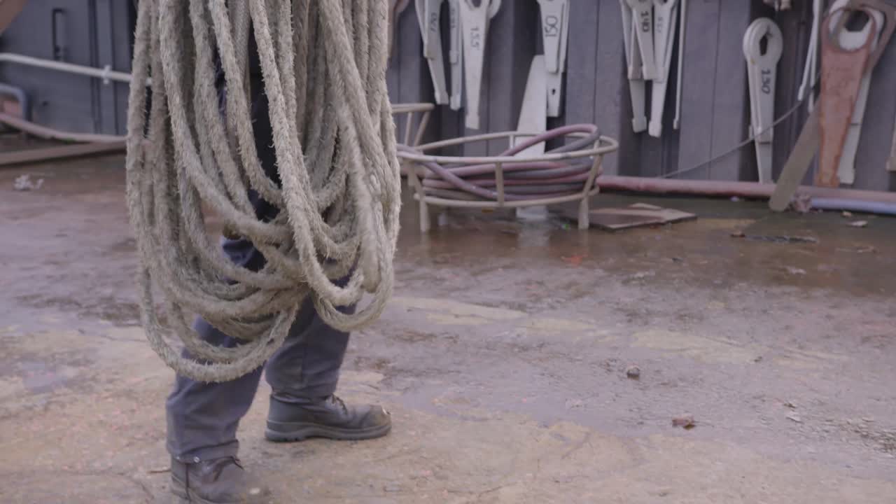 hombre en el puerto enrollando una cuerda náutica recogiéndola y alejándose