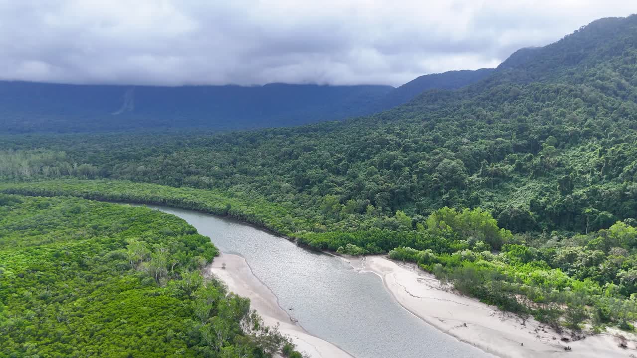 Drone glides above winding river, lush mangroves, and rainforest under cloudy daylight in Queensland