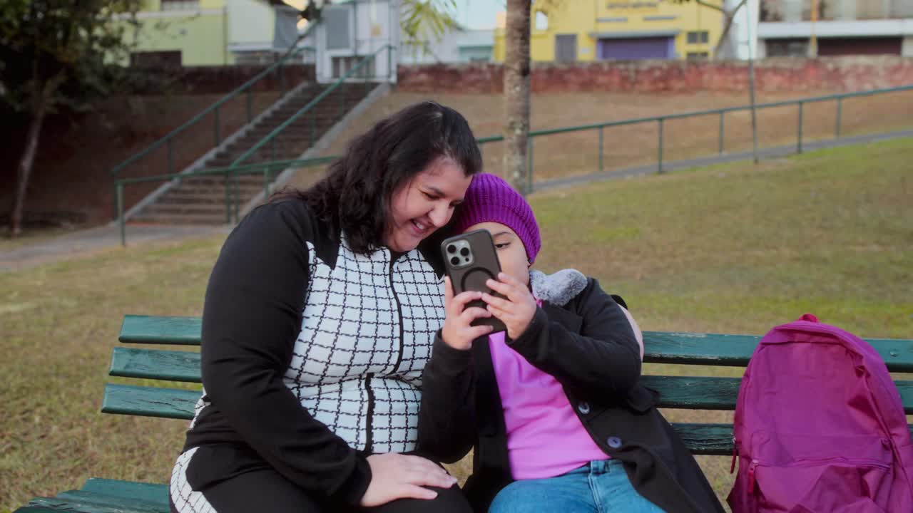 Woman and girl sharing a joyful moment with a smartphone in a park