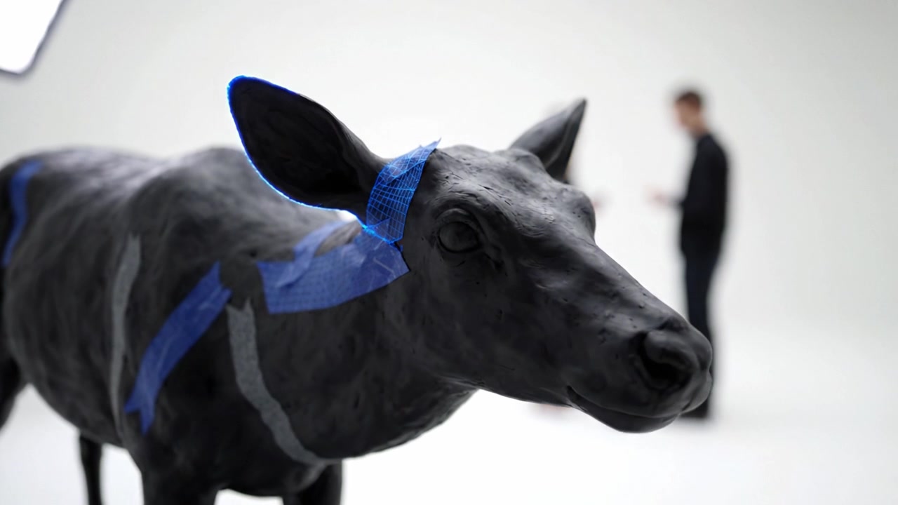 Innovative Black Cow Sculpture Showcasing 3D Texturing Techniques in an Artistic Environment with Figures Engaged in Discussion About the Artwork