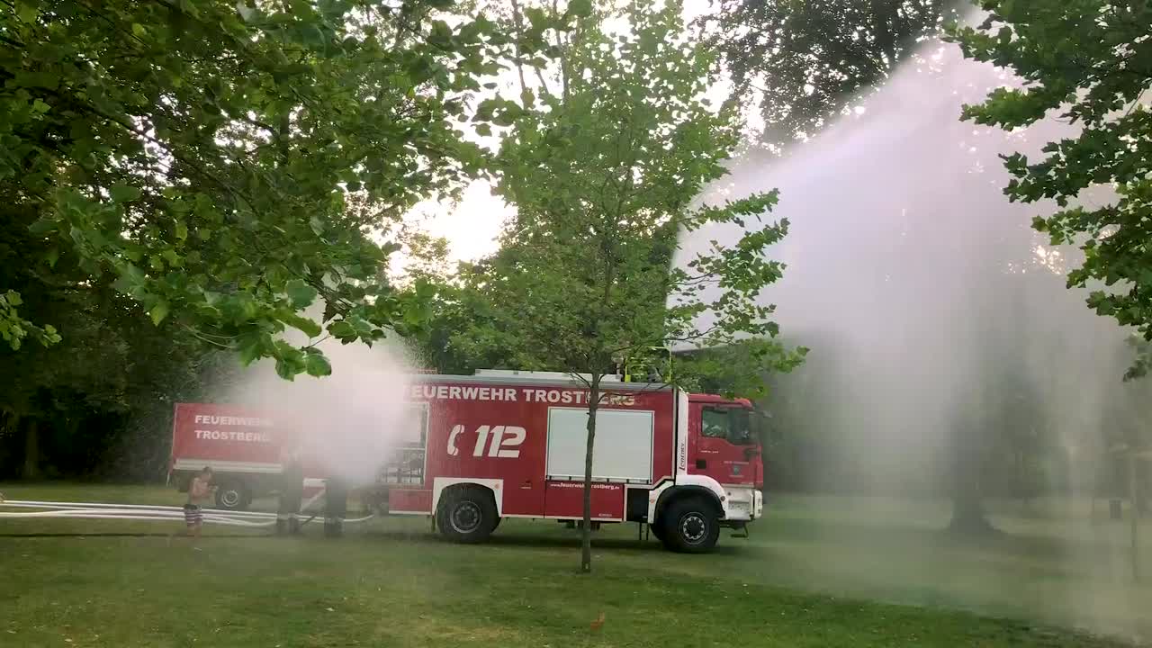 camión de bomberos alemán rociando agua para niños y árboles en un caluroso día de verano-9