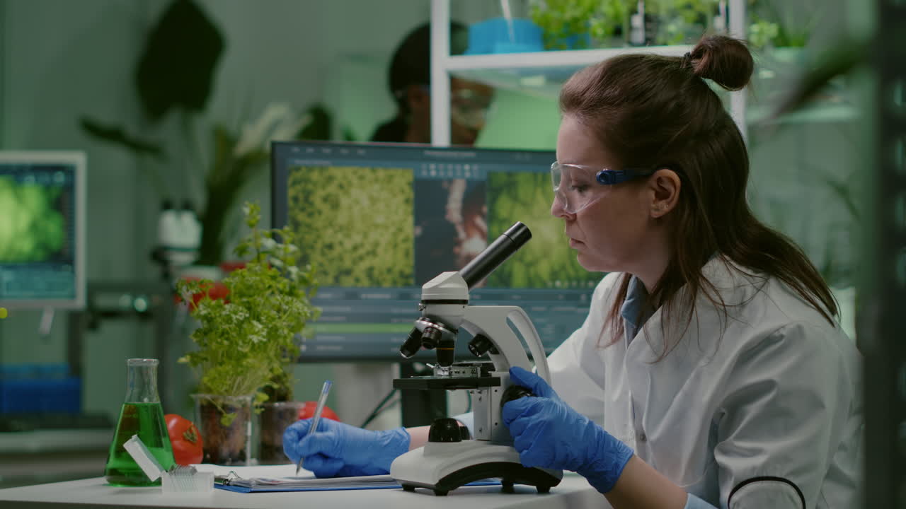 Pharmaceutical scientist looking at green leaf sample on microscope