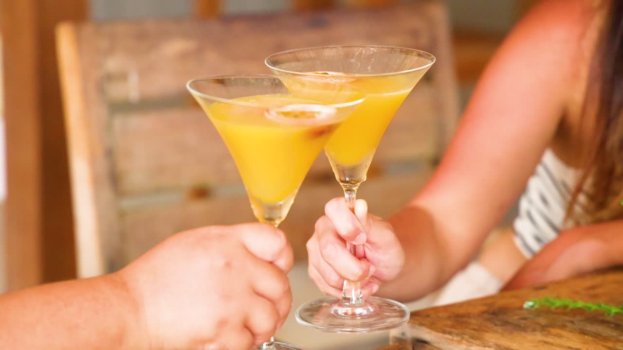 Two people clink glasses of vibrant orange cocktails in a warm, inviting setting with soft lighting