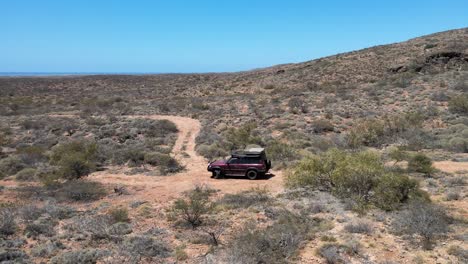 Luftaufnahme-Eines-4x4-Safarifahrzeugs,-Das-Bei-Sonnenlicht-Auf-Einer-Hügeligen-Wüste-Fährt