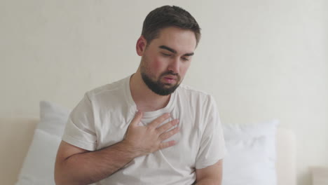 sick man sitting on bed having shortness of breath and touching his chest