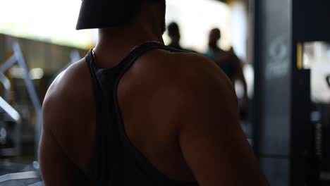 Young-strong-Caucasian-man-sitting-on-workout-bench-in-gym-pulling-weights-towards-chest-working-upper-body-and-shoulder-muscles,-close-up-pan