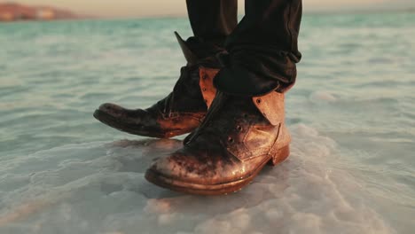 man with old leather boots stands on large salt outcrop in dead sea, israel