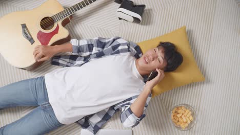 top view of asian teen boy talking on smartphone while lying on carpet on the floor at home