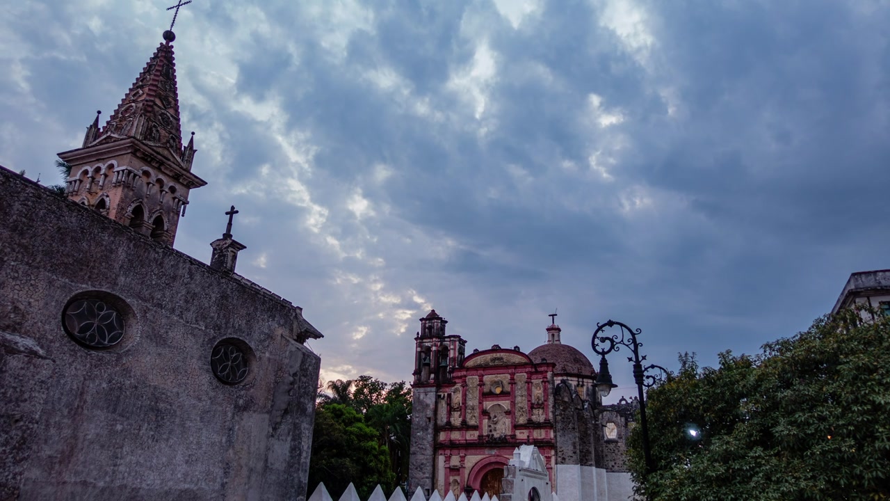 Static timelapse of clouds moving through sky at historic Cuernavaca Cathedral in Mexico during blue hour in the evening